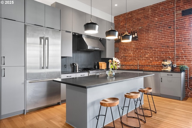 kitchen with a kitchen bar, a center island, hanging light fixtures, built in fridge, and exhaust hood