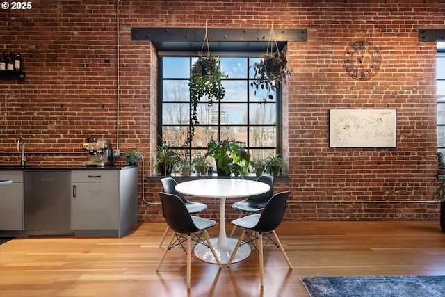 unfurnished dining area featuring brick wall, sink, and light hardwood / wood-style flooring