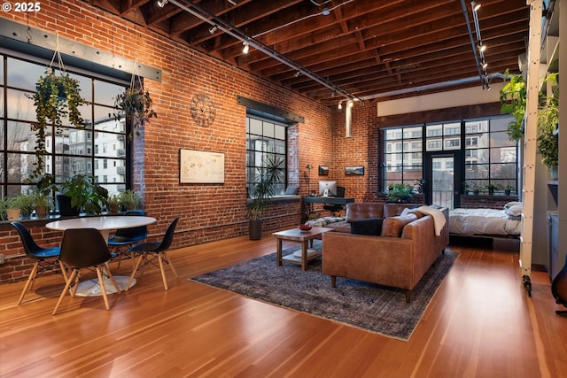 living room featuring hardwood / wood-style flooring, rail lighting, a high ceiling, and brick wall