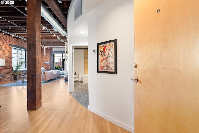 corridor with a towering ceiling, hardwood / wood-style flooring, and brick wall