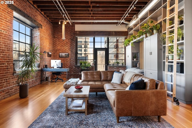 living room featuring a high ceiling, rail lighting, brick wall, and hardwood / wood-style floors