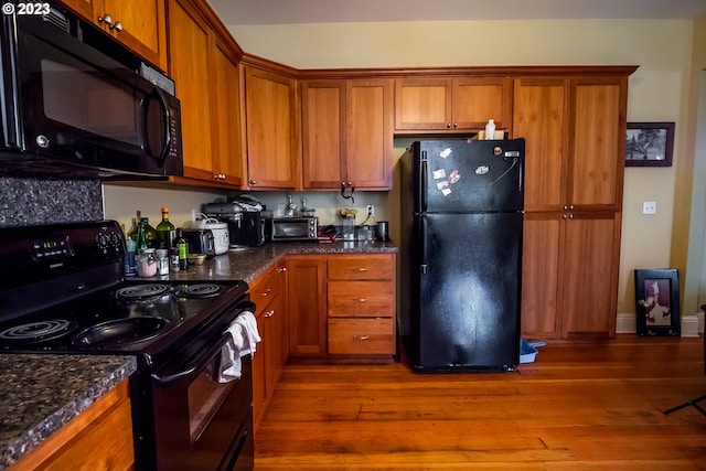 kitchen with dark wood finished floors, black appliances, brown cabinets, and dark stone counters