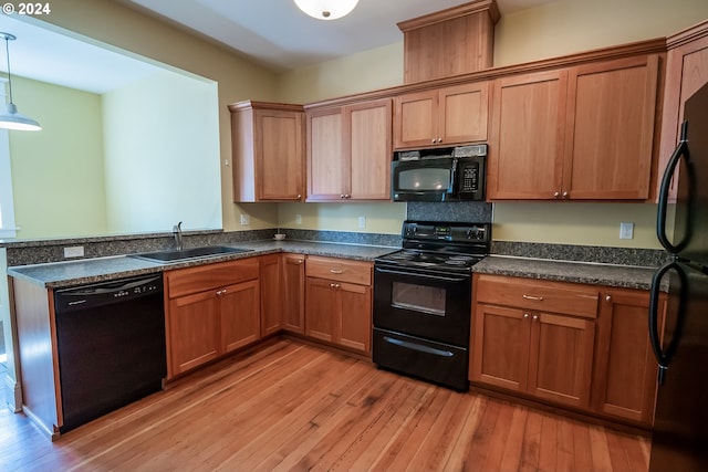 kitchen featuring black appliances, light wood-style flooring, a sink, decorative light fixtures, and dark countertops