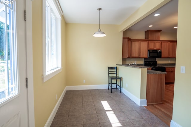 kitchen with brown cabinetry, a kitchen bar, a peninsula, tile patterned floors, and black appliances