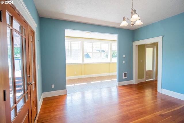 empty room featuring visible vents, a notable chandelier, wood finished floors, and baseboards