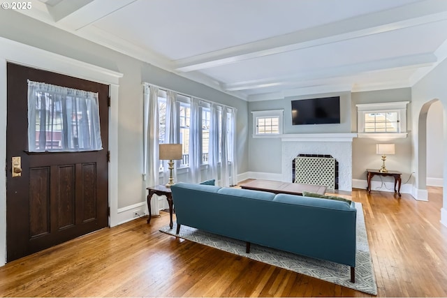 living area featuring arched walkways, beamed ceiling, a fireplace, and light wood-type flooring