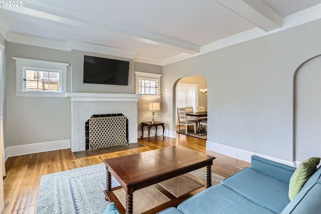 living room with arched walkways, beam ceiling, a tile fireplace, and wood finished floors