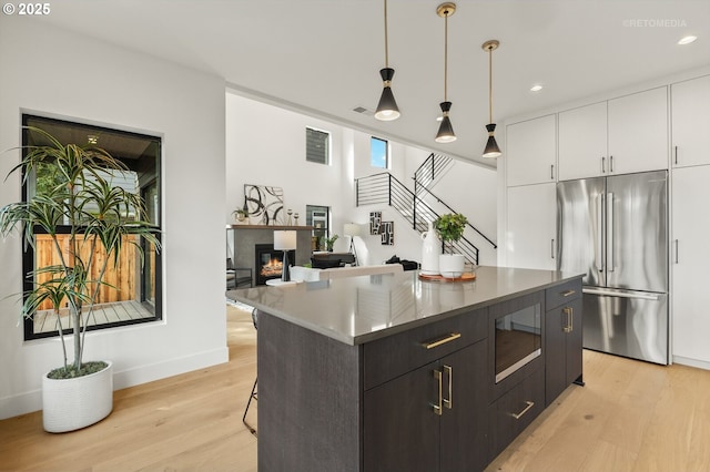 kitchen featuring built in microwave, decorative light fixtures, high end refrigerator, light wood-style floors, and white cabinets