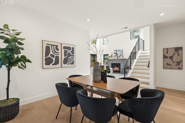 dining area with a glass covered fireplace, light wood-style flooring, baseboards, and visible vents