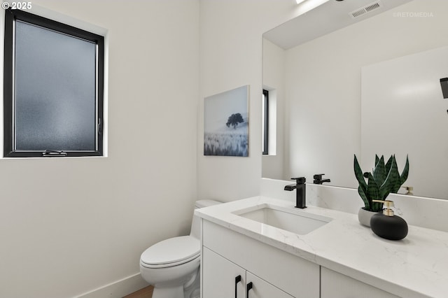 half bath featuring visible vents, baseboards, toilet, and vanity