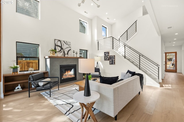 living room with a glass covered fireplace, stairway, a towering ceiling, and wood finished floors