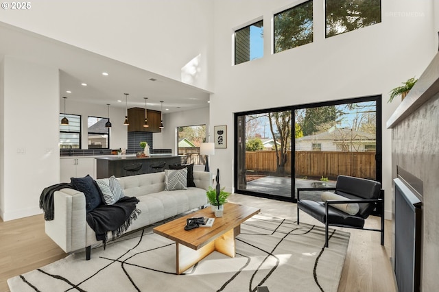 living area featuring recessed lighting, light wood-type flooring, baseboards, and a towering ceiling