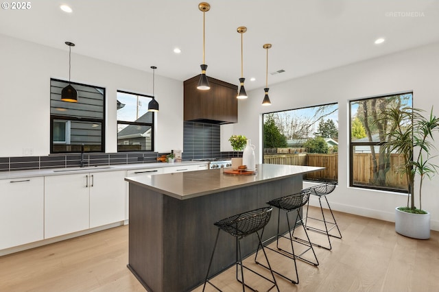 kitchen with light wood-style flooring, a sink, white cabinets, a kitchen bar, and a center island