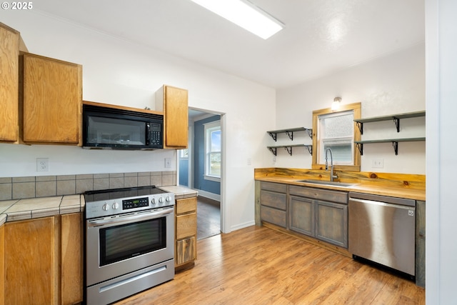 1006 Stillwell Ave, Tillamook, OR 97141 - kitchen with appliances with stainless steel finishes, a sink, open shelves, tile counters, and light wood-style flooring