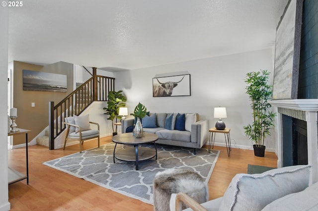 living room featuring stairs, baseboards, wood finished floors, and a fireplace