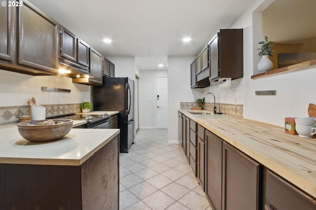 kitchen featuring light tile patterned flooring, a sink, dark brown cabinets, wood counters, and backsplash