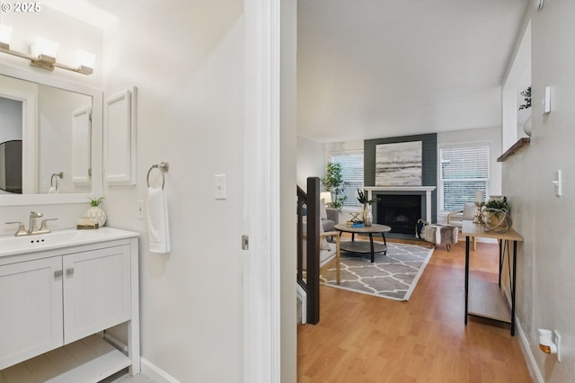 bathroom with a fireplace, vanity, wood finished floors, and baseboards