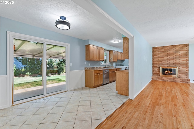 16880 Tracy Ave, Lake Oswego, OR 97035 - kitchen featuring stainless steel dishwasher, a textured ceiling, a wainscoted wall, a brick fireplace, and brown cabinetry
