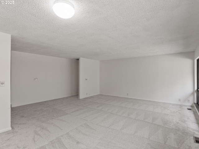 empty room with baseboards, light carpet, a textured ceiling, and visible vents
