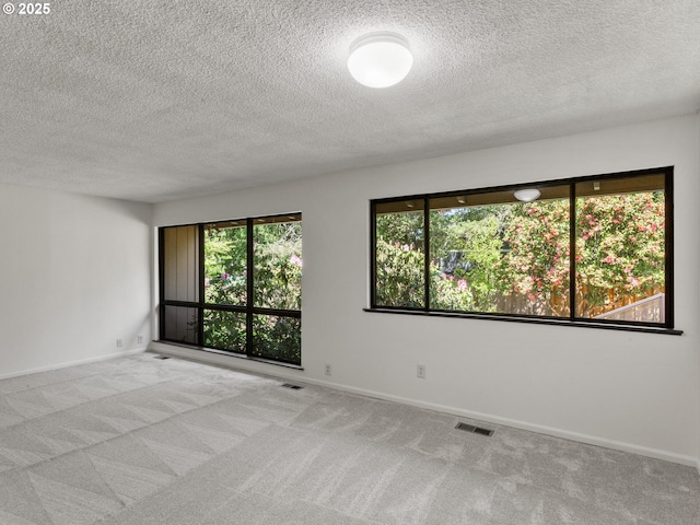 carpeted empty room featuring visible vents, a textured ceiling, and baseboards