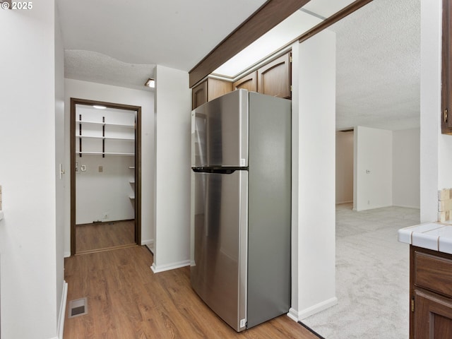 hallway with baseboards, light wood-type flooring, a textured ceiling, and visible vents