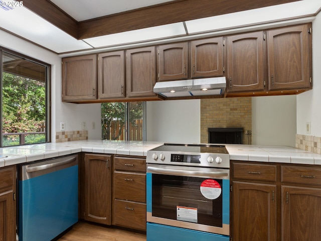 kitchen featuring a peninsula, dishwashing machine, under cabinet range hood, stainless steel electric stove, and light wood-style flooring