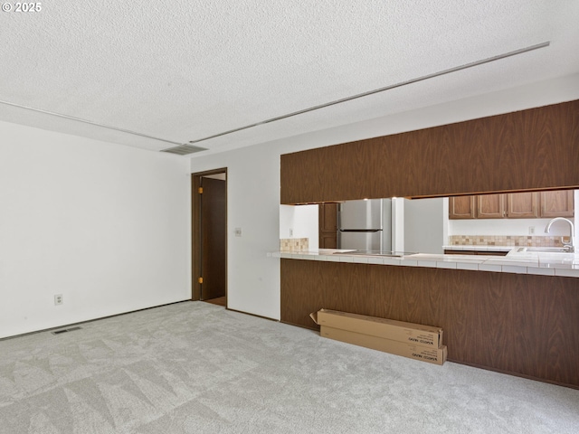 unfurnished living room with carpet floors, a textured ceiling, visible vents, and a sink