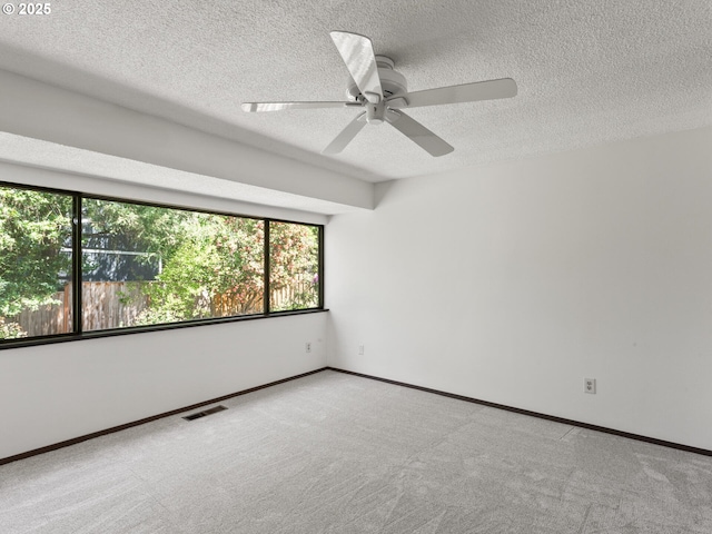 carpeted empty room featuring plenty of natural light, a textured ceiling, ceiling fan, and visible vents