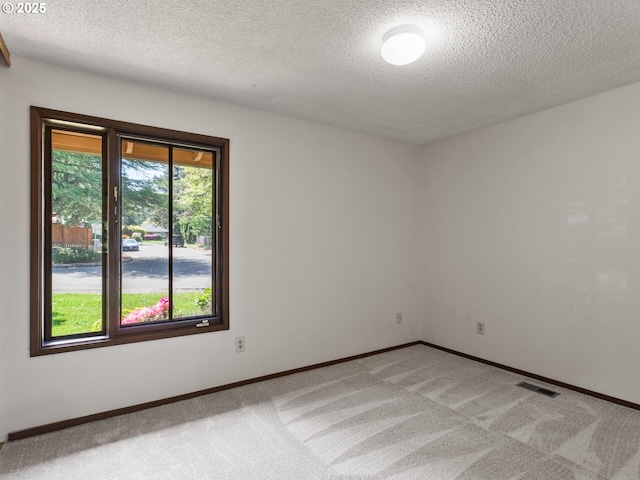 empty room featuring baseboards, light carpet, a textured ceiling, and visible vents