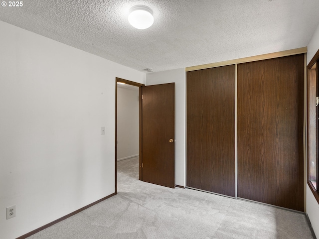 unfurnished bedroom featuring a closet, carpet flooring, a textured ceiling, and baseboards