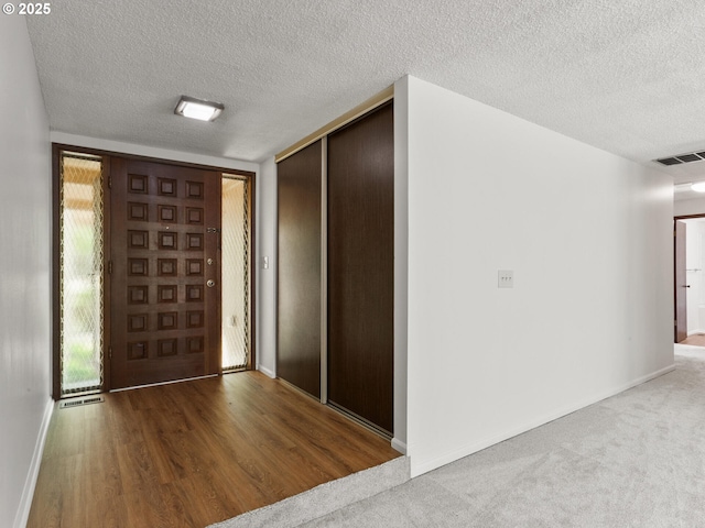foyer entrance with baseboards, wood finished floors, a textured ceiling, and visible vents