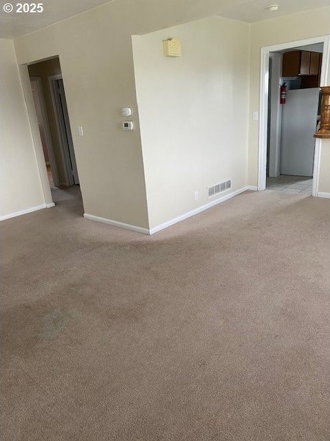 unfurnished room with light carpet, visible vents, and baseboards