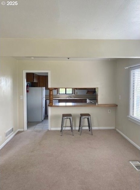 kitchen featuring visible vents, baseboards, light colored carpet, a breakfast bar, and freestanding refrigerator