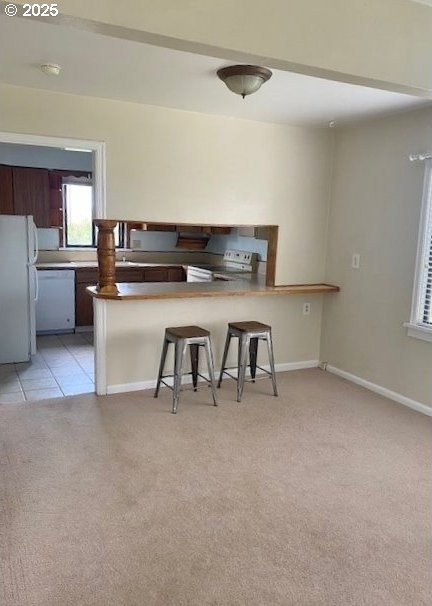 kitchen featuring baseboards, a breakfast bar, light carpet, a peninsula, and white appliances