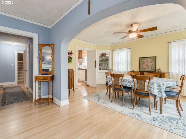 dining space with arched walkways, light wood-type flooring, ornamental molding, healthy amount of natural light, and a ceiling fan