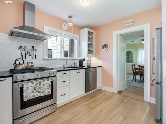 4415 SE Stark St, Portland, OR 97215 - kitchen with appliances with stainless steel finishes, wall chimney range hood, dark countertops, white cabinetry, and light wood-style flooring
