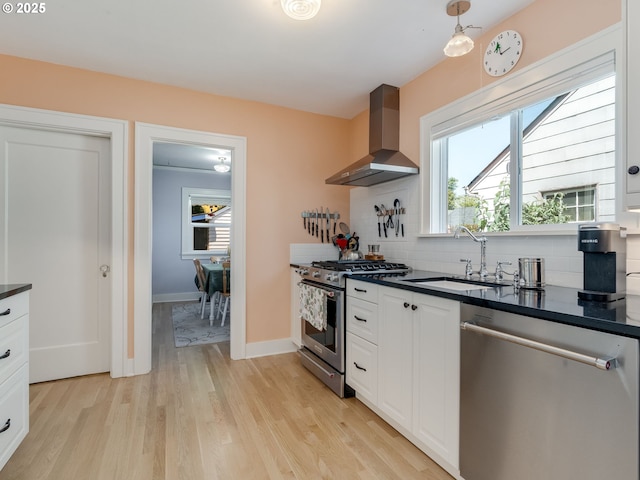 4415 SE Stark St, Portland, OR 97215 - kitchen with stainless steel appliances, wall chimney exhaust hood, dark countertops, light wood-type flooring, and white cabinets