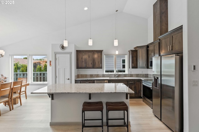 822 Spyglass Dr, Bandon, OR 97411 - kitchen with stainless steel appliances, high vaulted ceiling, dark brown cabinets, a center island, and light wood-type flooring