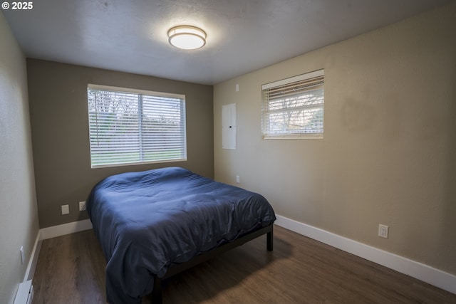 bedroom with multiple windows, a baseboard heating unit, baseboards, and wood finished floors