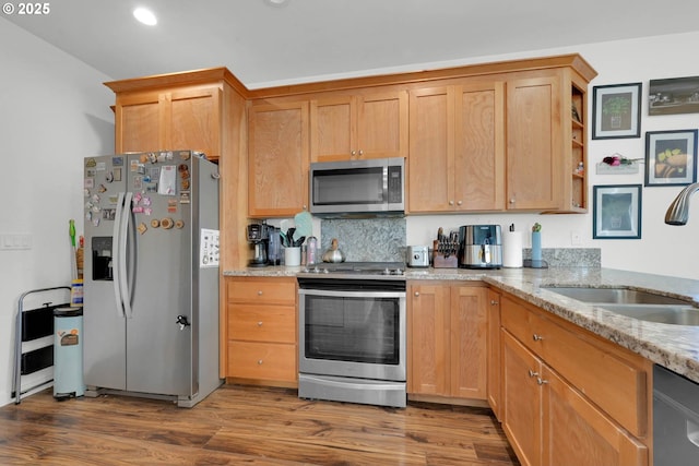 kitchen with light stone counters, stainless steel appliances, sink, and hardwood / wood-style floors