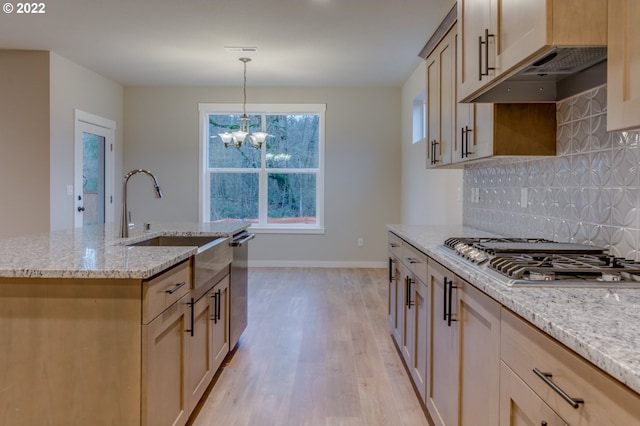 kitchen with decorative backsplash, appliances with stainless steel finishes, light stone counters, light wood finished floors, and a chandelier