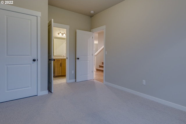 unfurnished bedroom with baseboards, light colored carpet, and ensuite bath