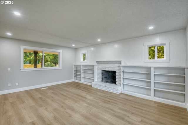 unfurnished living room featuring a brick fireplace, light hardwood / wood-style flooring, and a textured ceiling