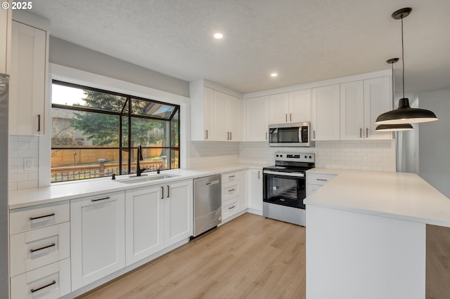 kitchen featuring white cabinets, decorative light fixtures, stainless steel appliances, sink, and kitchen peninsula