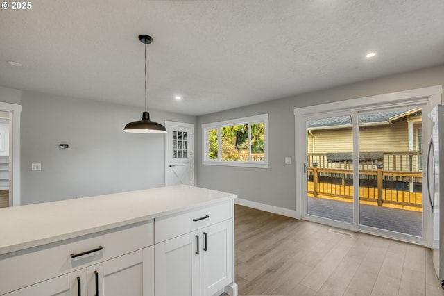 kitchen featuring light wood-type flooring, pendant lighting, stainless steel fridge, and white cabinetry