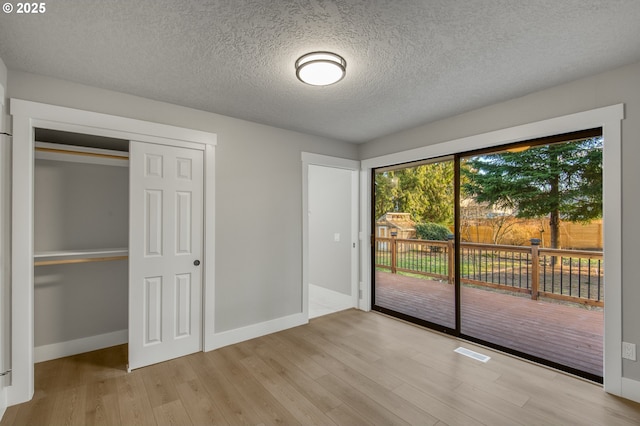 unfurnished bedroom with light hardwood / wood-style floors, a textured ceiling, a closet, and access to outside