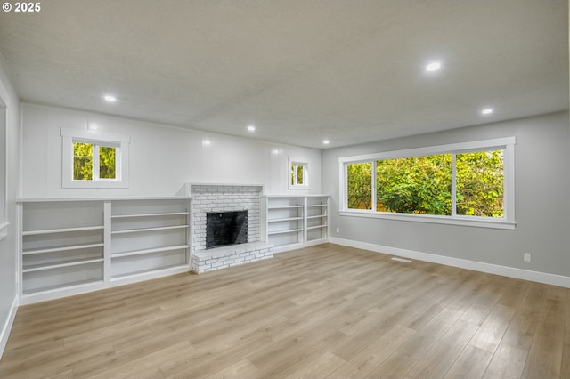 unfurnished living room featuring a brick fireplace, light hardwood / wood-style floors, and a textured ceiling