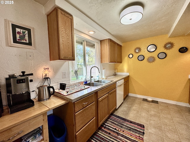 kitchen featuring a textured ceiling, brown cabinets, a sink, and baseboards