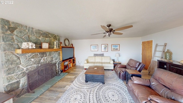 living room with ceiling fan, light wood-type flooring, a fireplace, and a textured ceiling