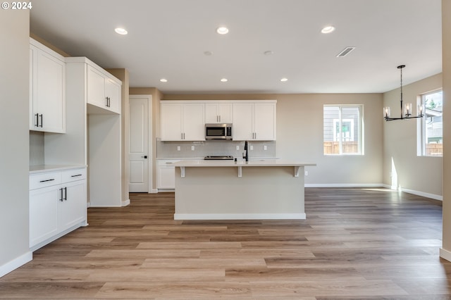 kitchen featuring white cabinets, light hardwood / wood-style floors, and a center island with sink